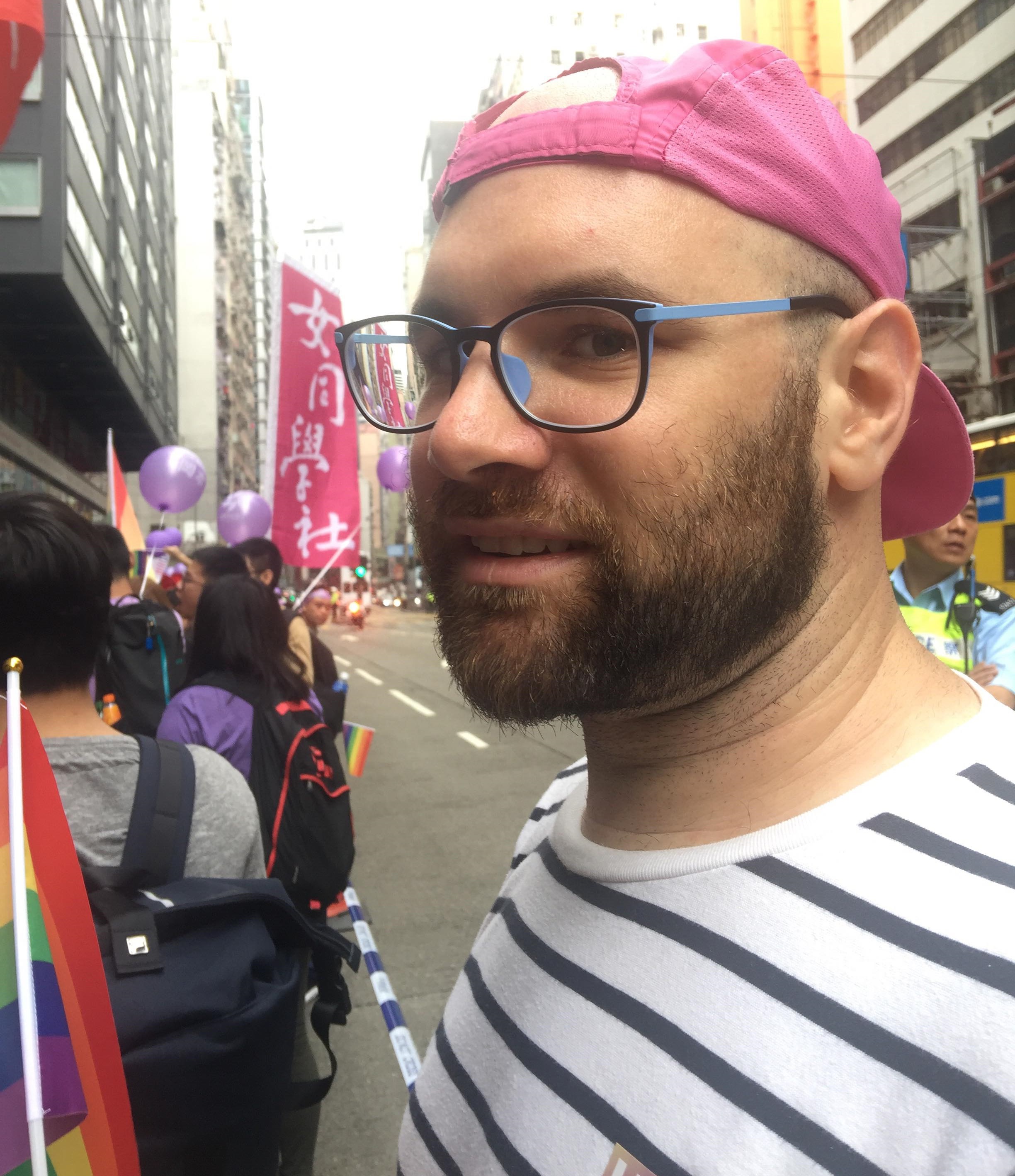 An image of the creator in this page: a Caucasian man with glasses, a short beard, and wearing a pink cap backwards. In the background of the image is a sign that reads 女同學社